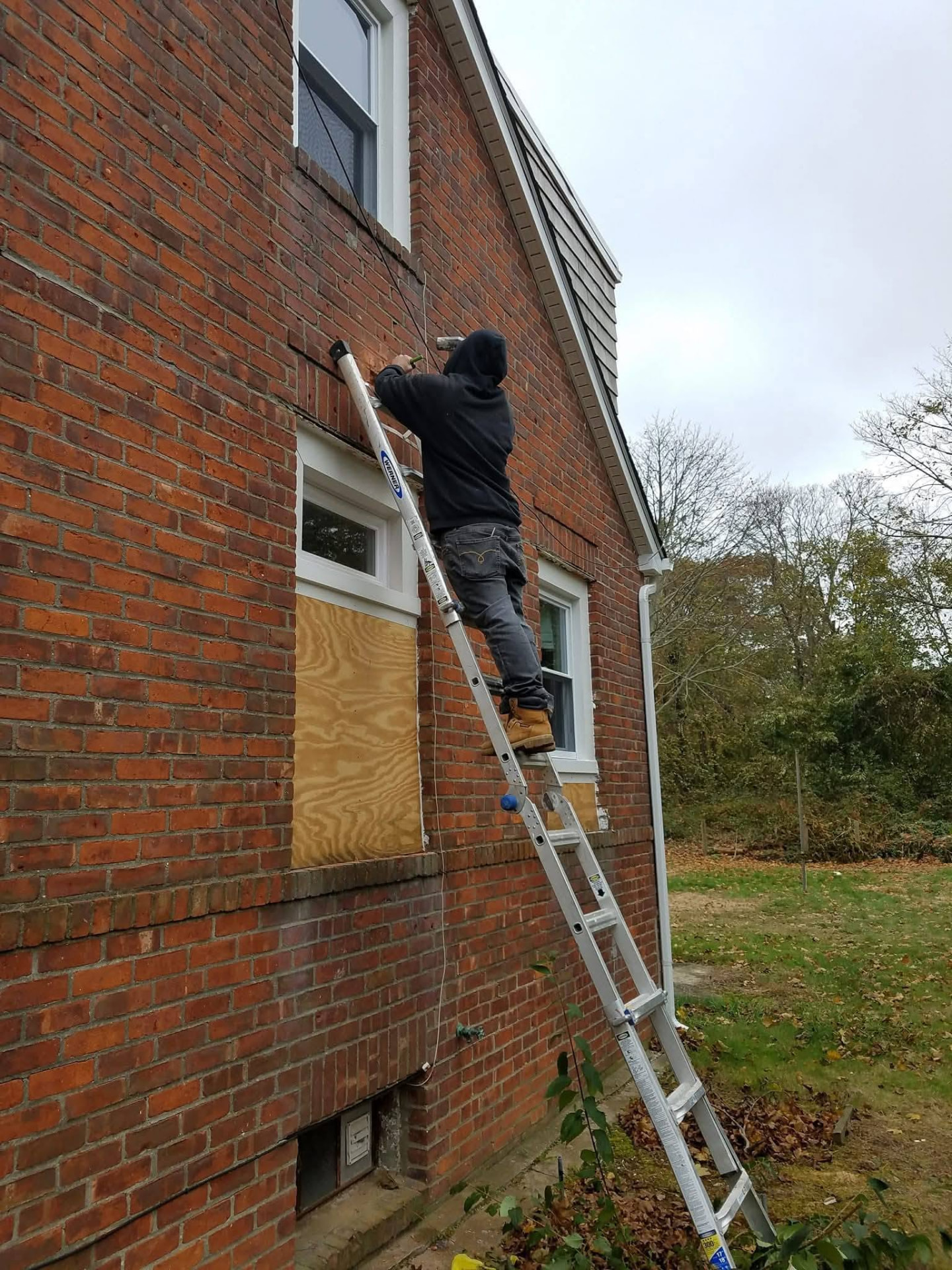Worker on an extension ladder replacing windows on a brick home