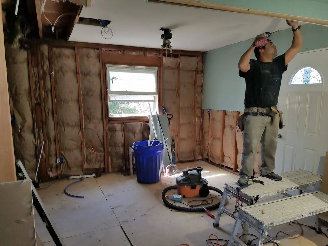 Crew member cutting drywall overhead in a room stripped to insulation and framing