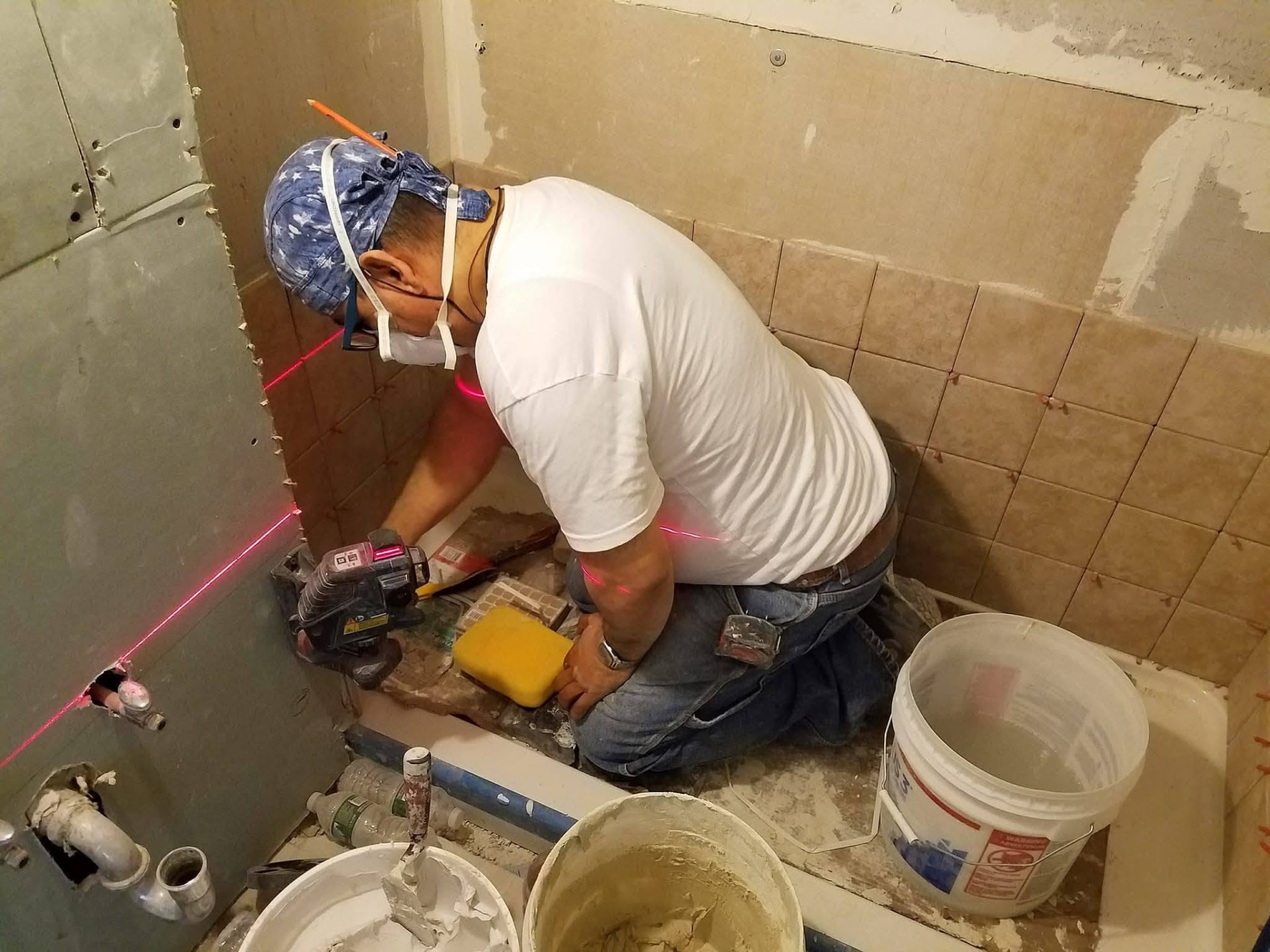 Tile setter using a laser level while installing bathroom wall tile