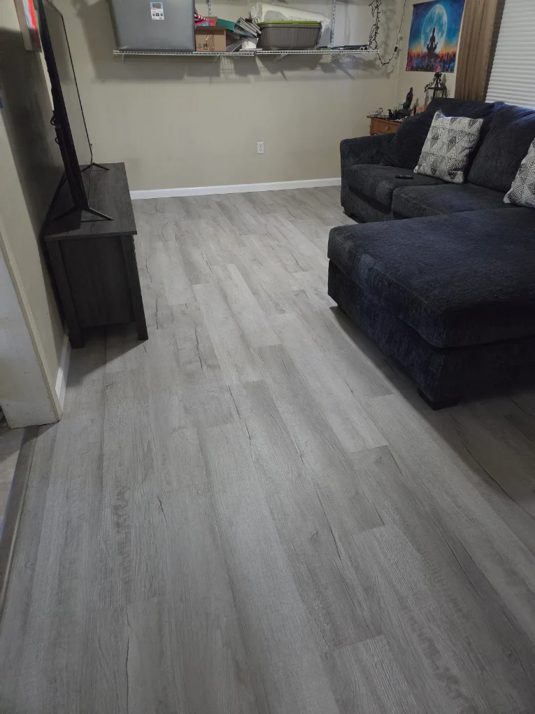 Finished grey luxury vinyl plank flooring running through a living room with a sectional sofa