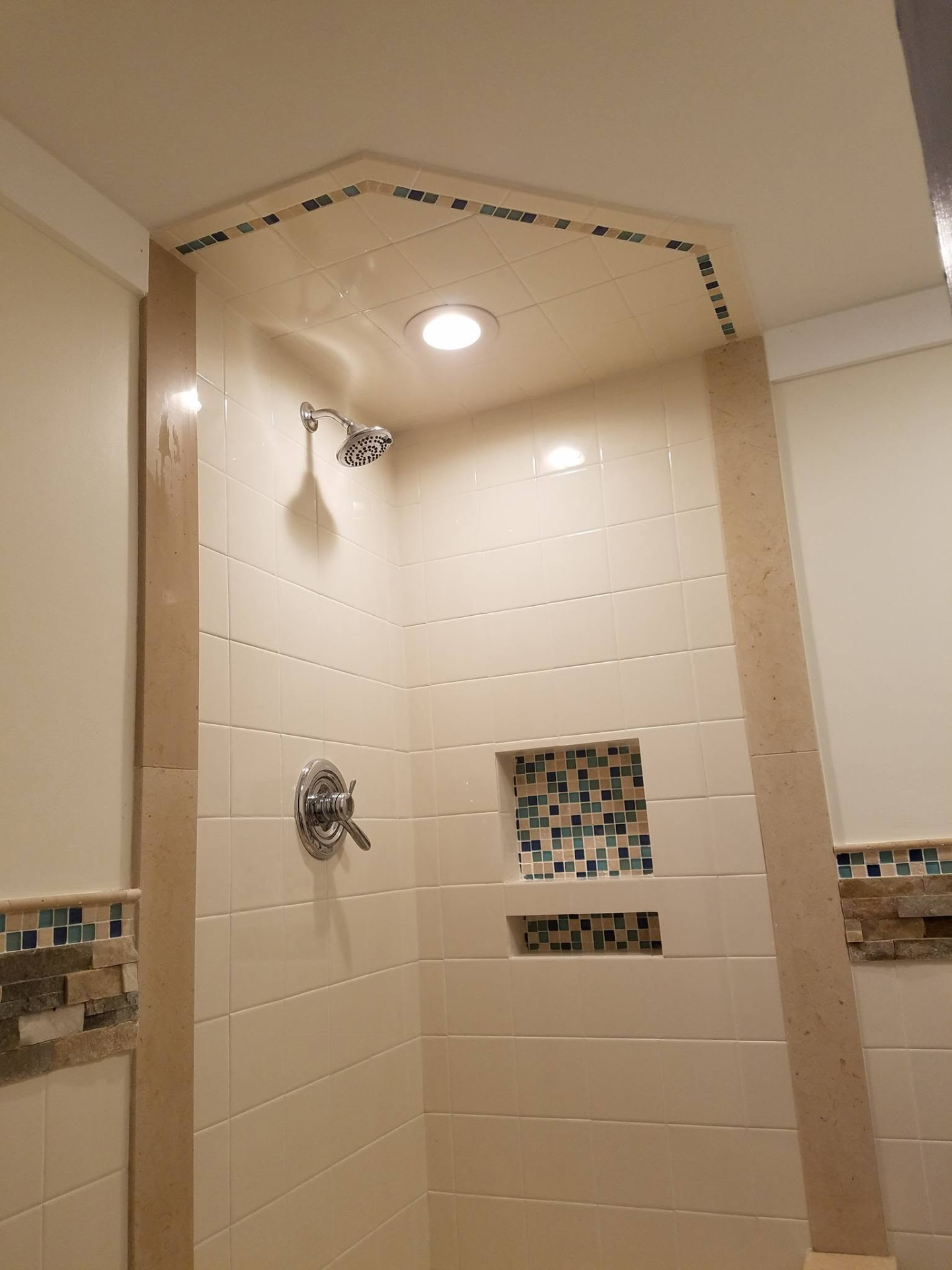 Finished tiled shower with mosaic glass accent band, recessed niches and marble trim