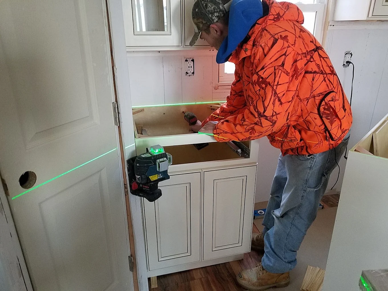 Carpenter setting a base cabinet to a green laser line during a kitchen install