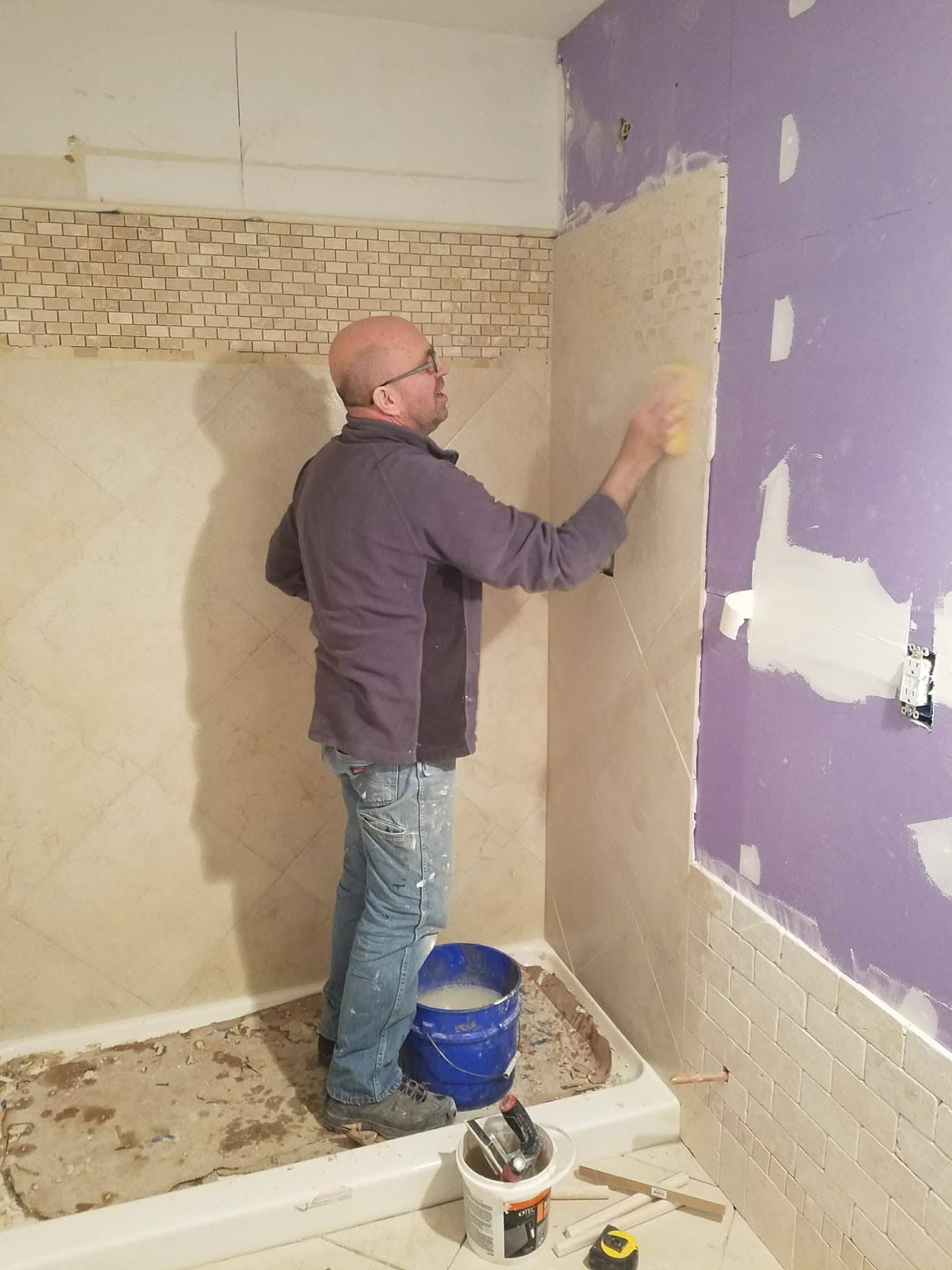 Craftsman sponging fresh grout on newly installed shower wall tile