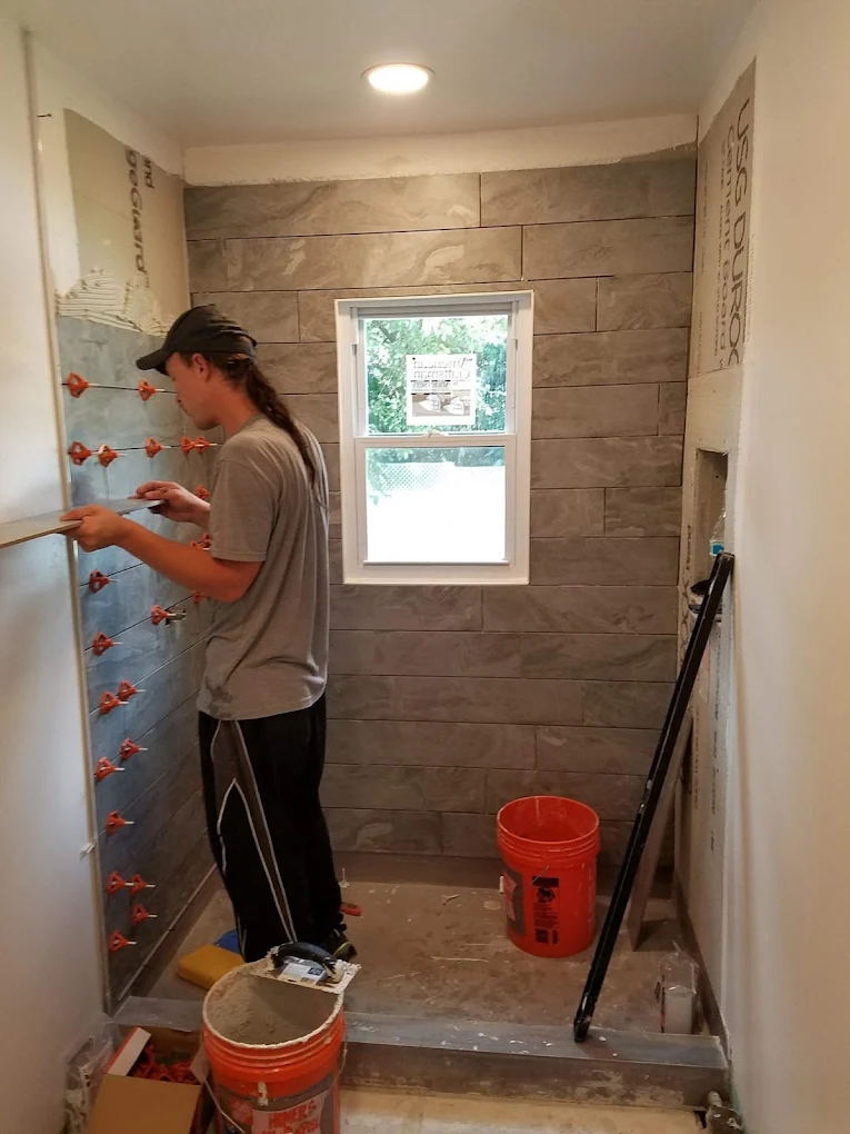 Tile setter leveling large-format shower wall tile with clips beside a bathroom window
